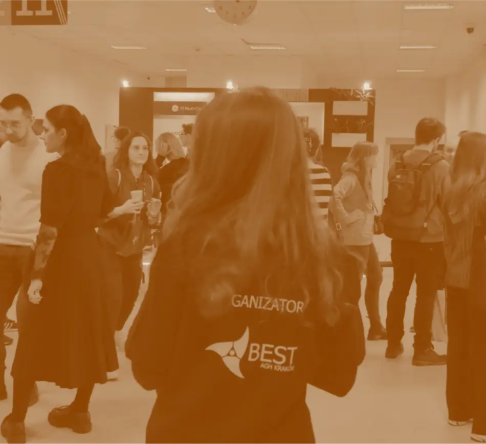 Kobieta tyłem w koszulce z napisem „ORGANIZATOR” i logo BEST AGH Kraków na tle tłumu uczestników wydarzenia.