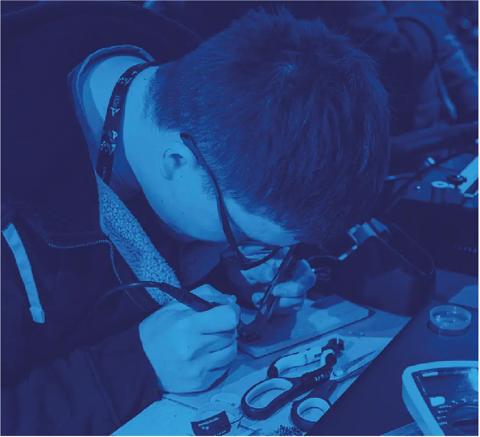 Skupiony student w okularach precyzyjnie lutujący komponenty na płytce drukowanej w kategorii Robotyka.
